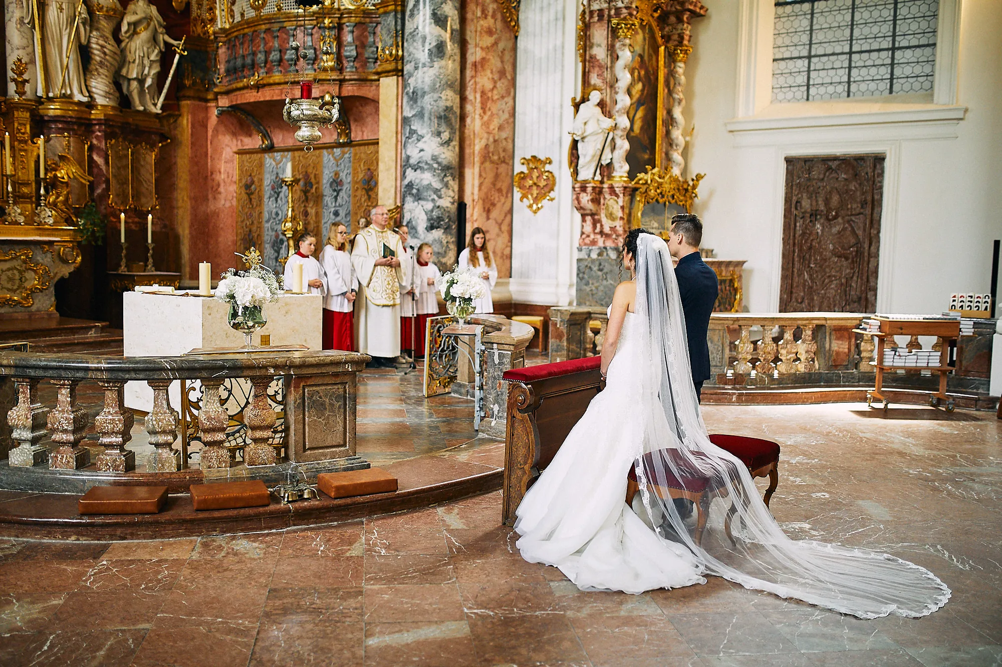 Braut mit langem Schleier in einer Barockkirche bei der kirchlichen Trauung – Hochzeitsfotos von Reinhard Fürstberger