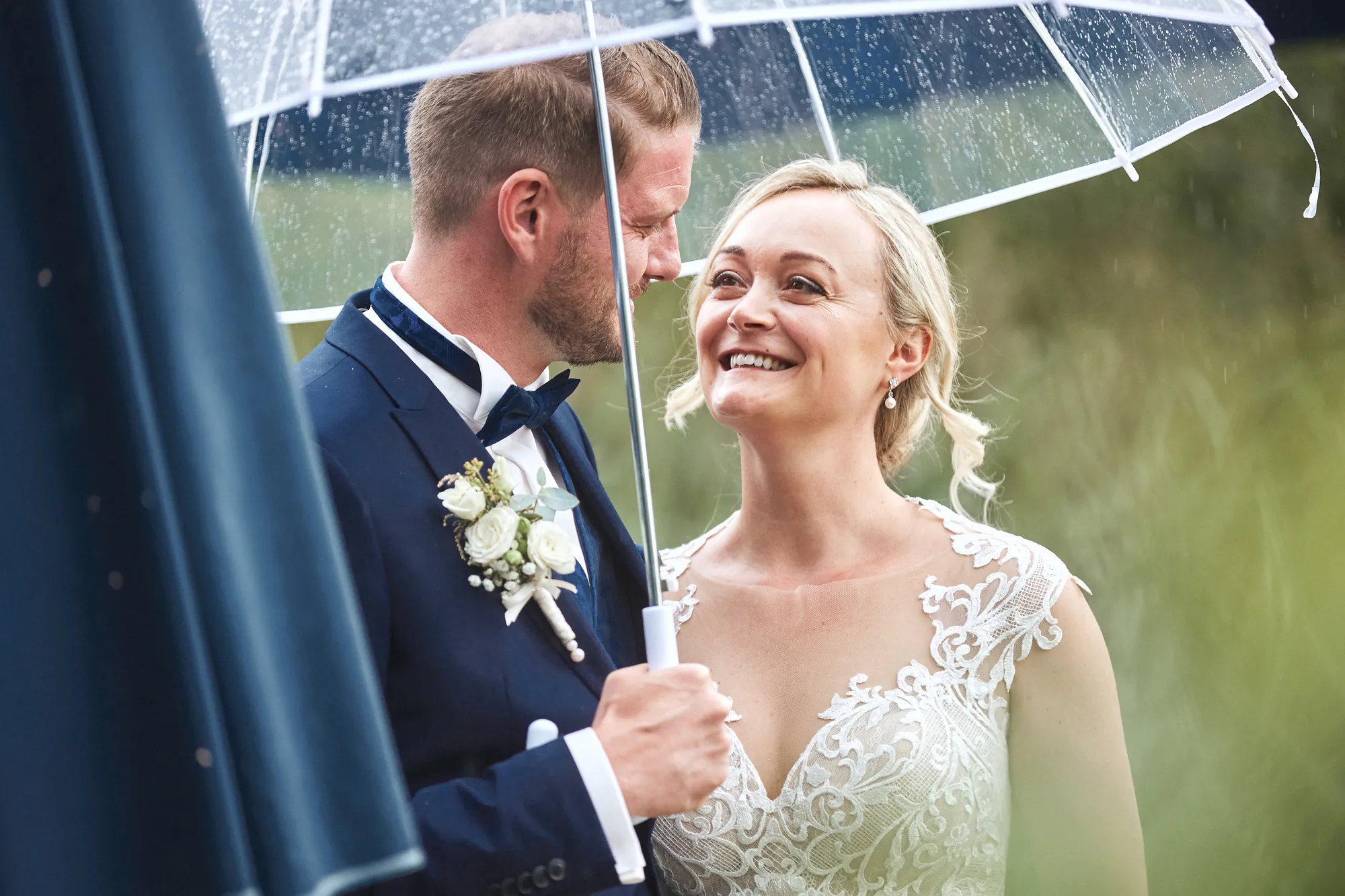 Lachendes Brautpaar unter einem durchsichtigen Regenschirm – Hochzeitsfotos von Reinhard Fürstberger