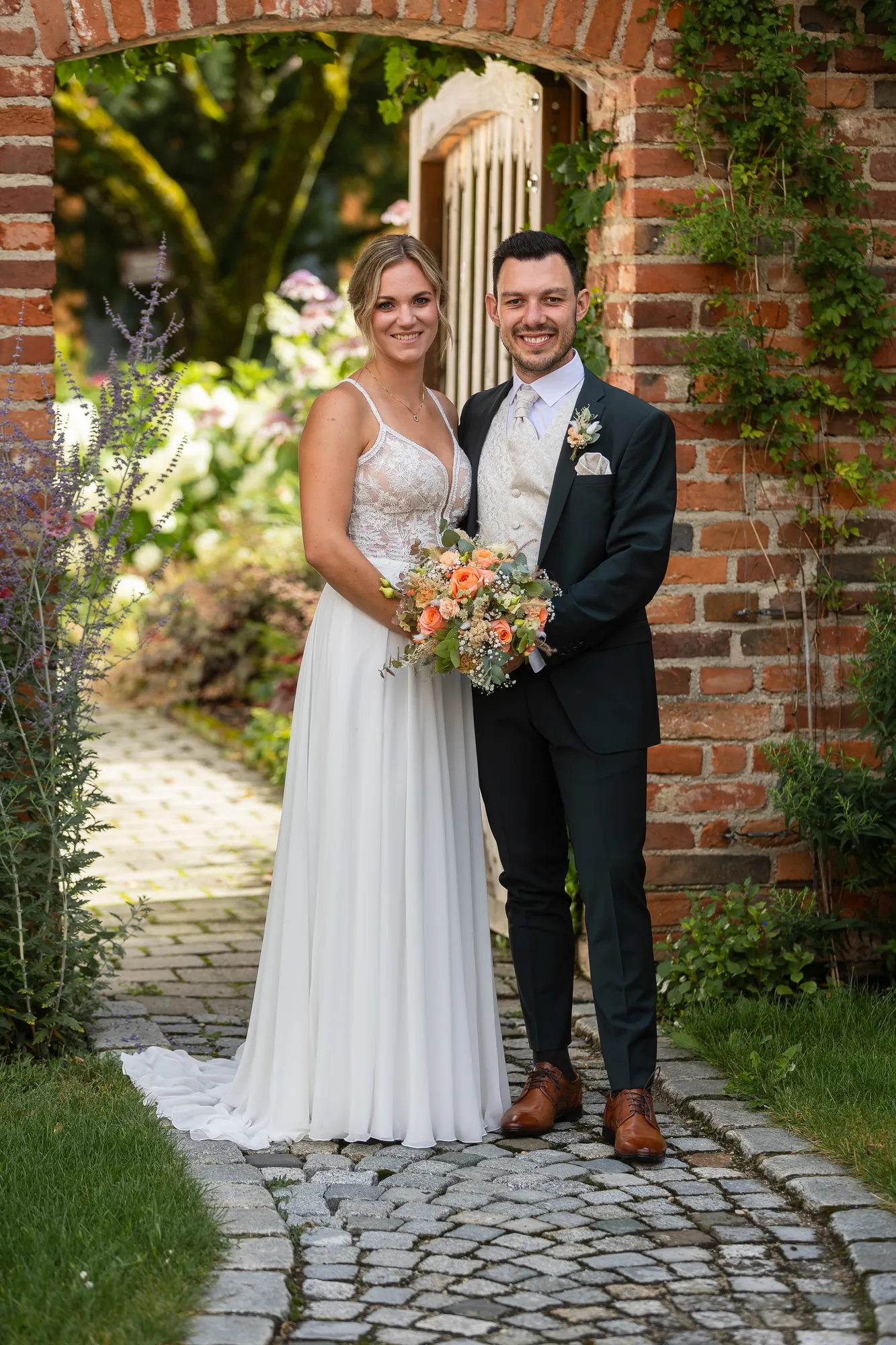 Brautpaar mit Brautstrauß unter einem Torbogen – Hochzeitsfotograf aus Niederbayern