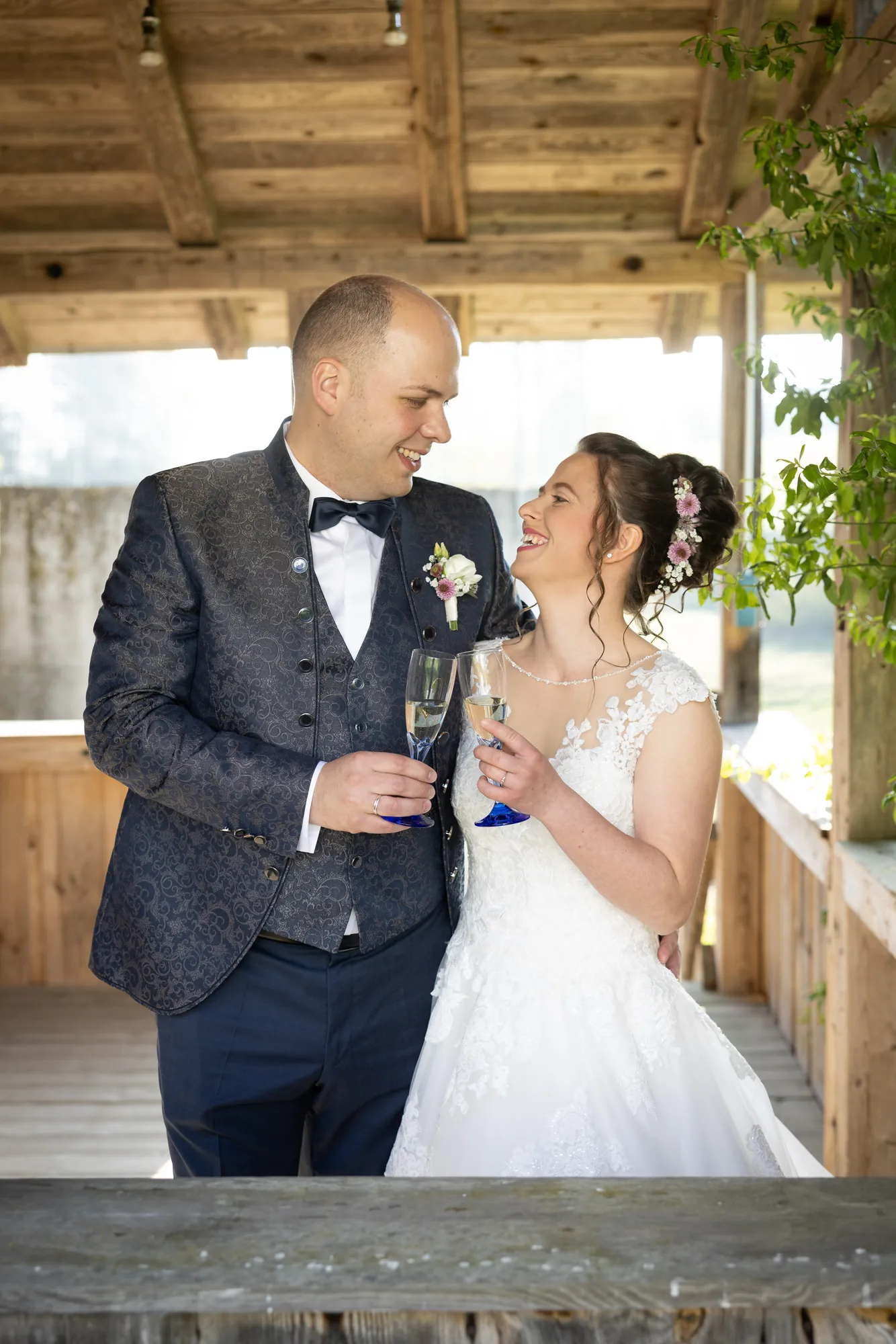 Brautpaar beim Anstoßen unter einem Holzdach – Hochzeitsfotograf aus Niederbayern